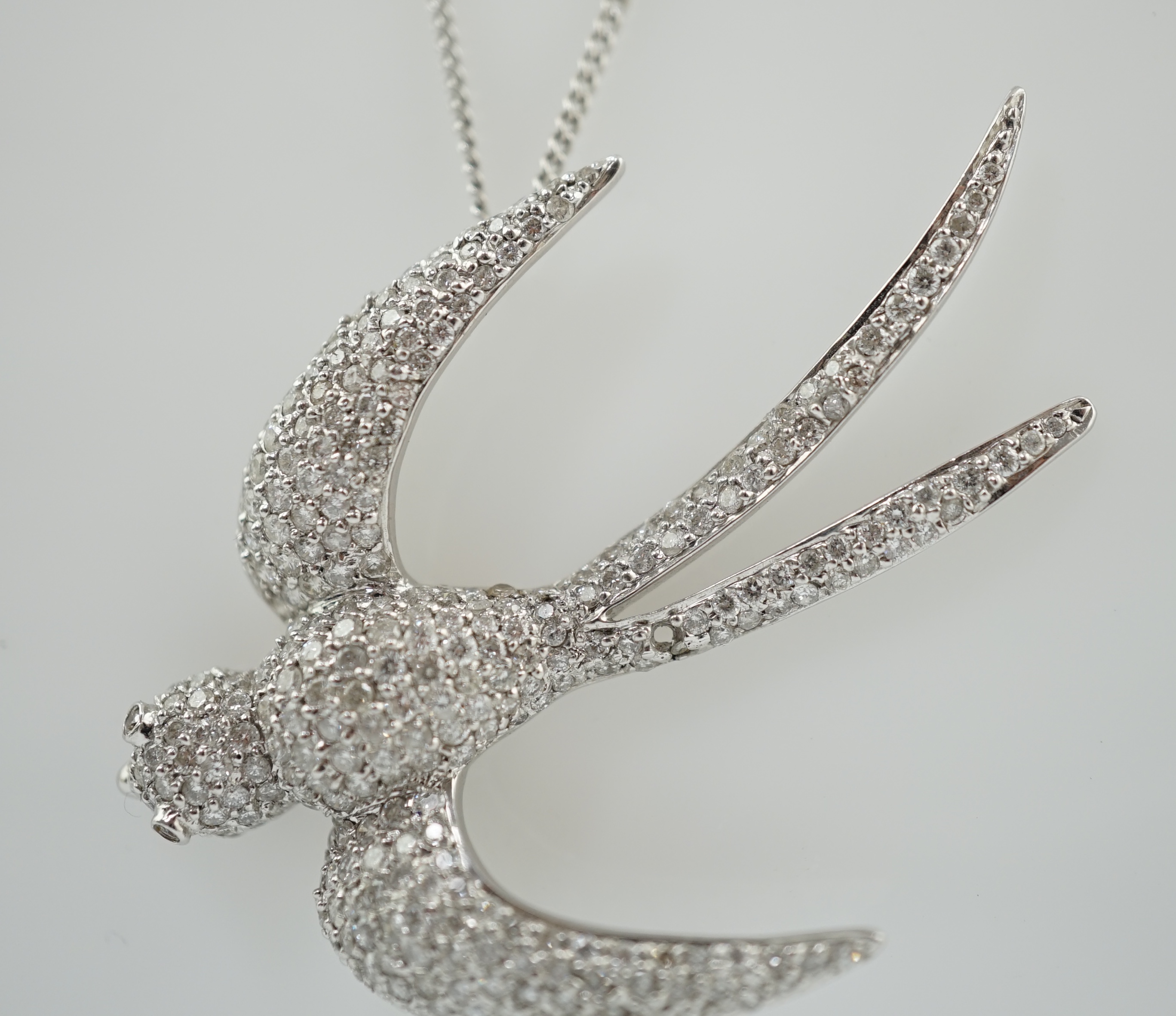 A modern 18k white gold and pavé set diamond pendant, modelled as a swallow, on an 18ct white gold fine link chain